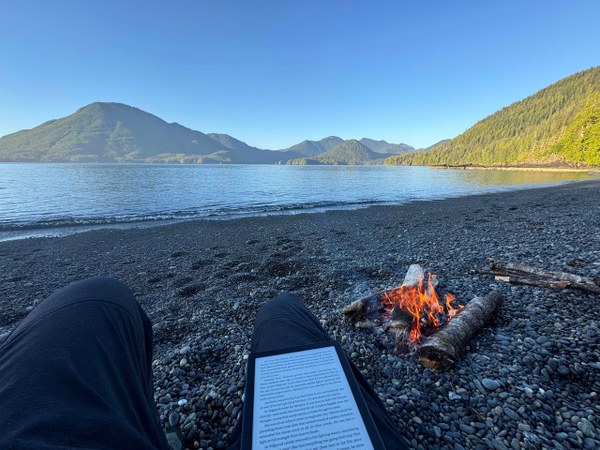 Text on a kindle in the foreground.  Water and tree covered hills in the distance.