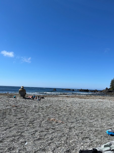 A pebble beach, blue sky, and a person sitting in a camp chair