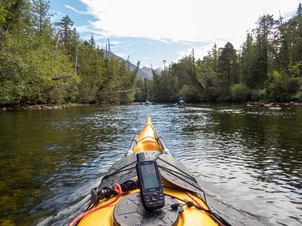 View forward over a sea kayak deck to a river with trees along the bank